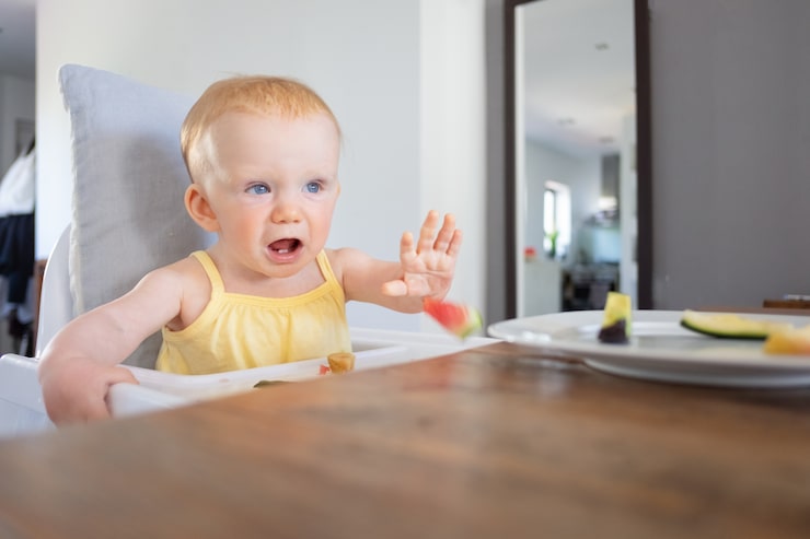 annoyed-cute-baby-sitting-highchair-throwing-slices-fruits-first-solid-food-child-care-concept_74855-6739