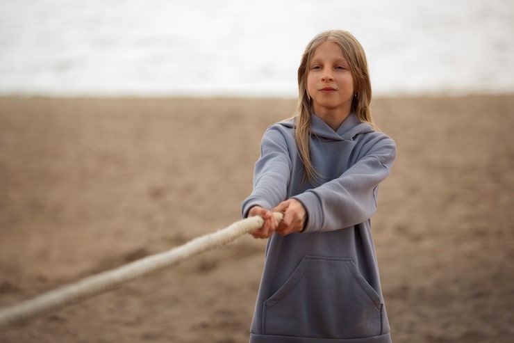 medium-shot-girl-playing-tug-war-beach_23-2150417360