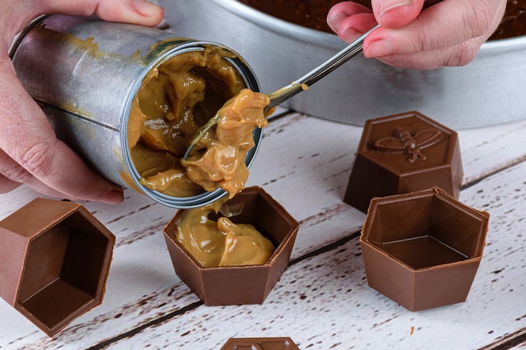 closeup-confectioner-putting-spoon-dulce-de-leche-small-chocolate-molds-make-brazilian-honey-cake_292824-1053