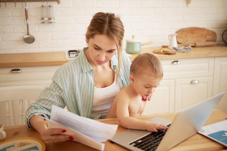 serious-concentrated-young-female-studying-papers-hands-paying-bills-online-sitting-kitchen-table-front-open-laptop-holding-baby-son-her-lap-little-child-typing-portable-computer_344912-19